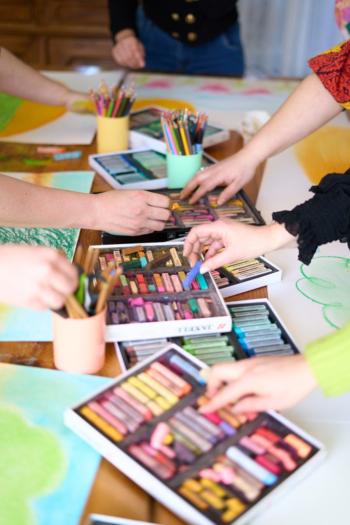 Des mains de participants à une séance d'art thérapie évolutive prenant des pastels pour dessiner.